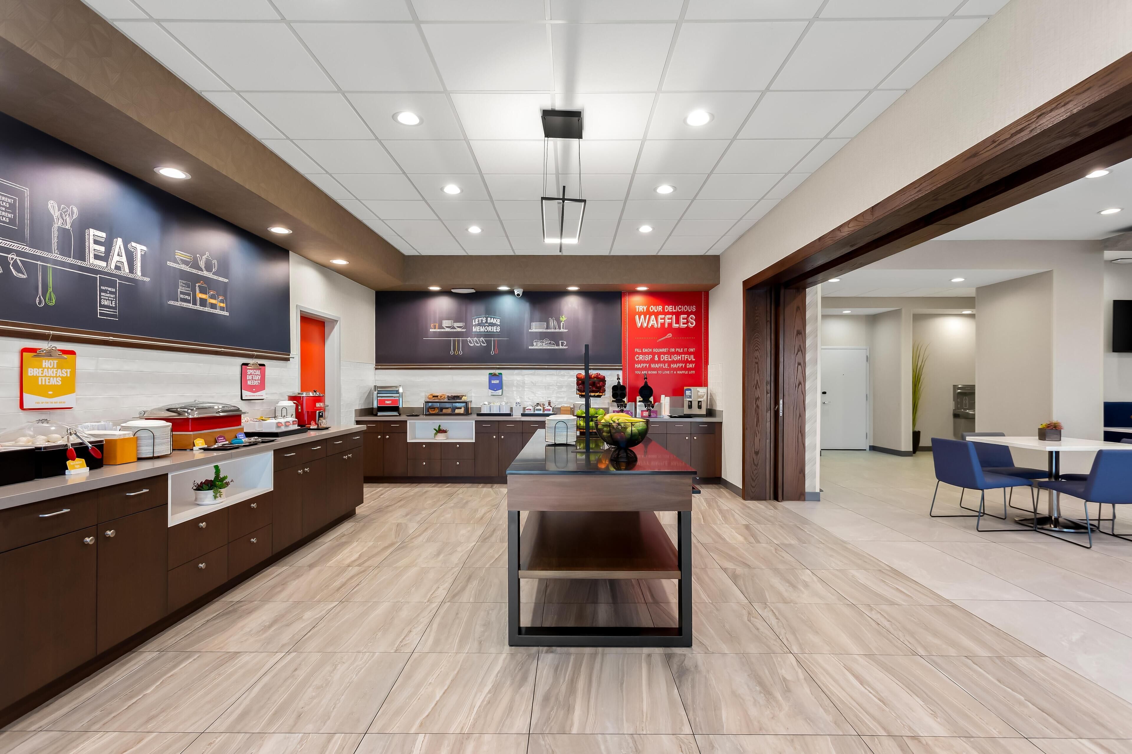 A modern kitchen area with a central island, a counter with food items, and a wall with menu options.