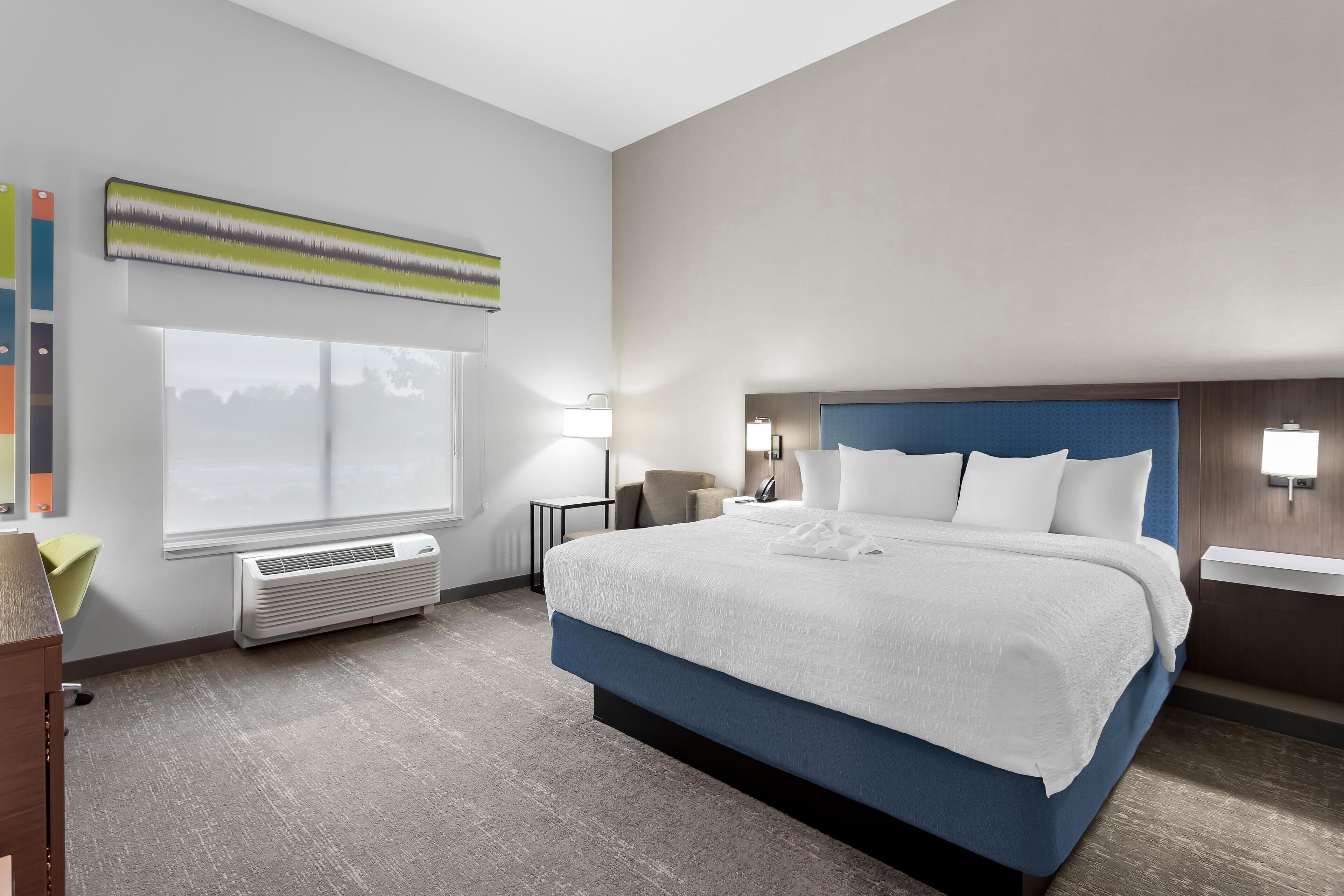 Une chambre d’hôtel moderne avec un grand lit, une fenêtre donnant sur un beau paysage, un bureau et une chaise.
