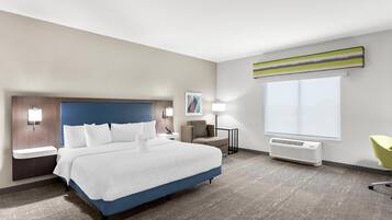 Una habitación de hotel moderna con una cama grande, mesitas de noche, un escritorio, una silla, un ventanal y un aire acondicionado instalado en la pared.