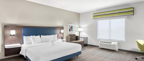 Una habitación de hotel moderna con una cama grande, mesitas de noche, un escritorio, una silla, un ventanal y un aire acondicionado instalado en la pared.
