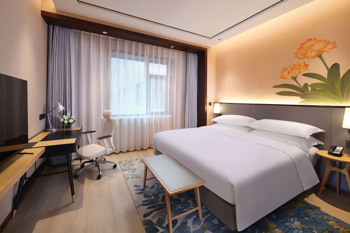 A hotel room with a bed, desk, chair, and a TV.
