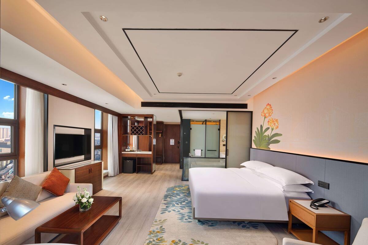 A modern hotel room with a large bed, a desk, a TV, and a city view.