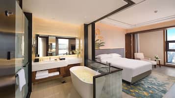 Una habitación de hotel moderna con una cama grande, baño independiente con bañera, tocador con espejo y un amplio ventanal con vistas a la ciudad.