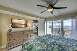 Une chambre avec un lit, un ventilateur de plafond, un téléviseur fixé au mur, une commode et une vue sur l’extérieur grâce à de grandes fenêtres.