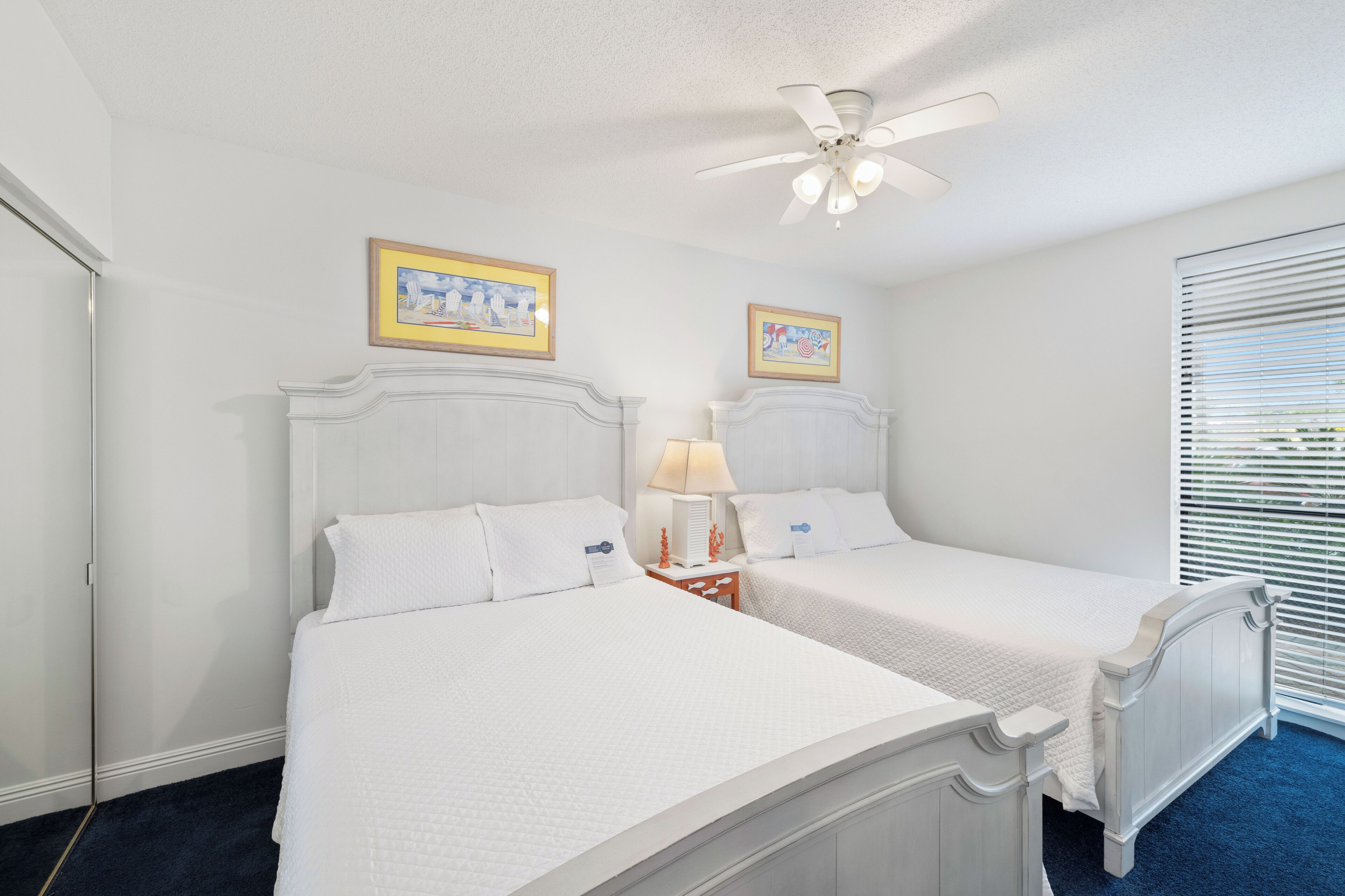 A bedroom with two beds, a ceiling fan, and two framed pictures on the wall.