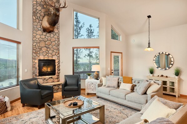 A spacious living room with a stone fireplace, leather armchairs, a grey sofa, and a large mirror.