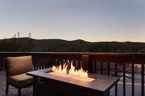 Une terrasse agrémentée d’un foyer, d’un fauteuil et offrant une vue sur une colline boisée.