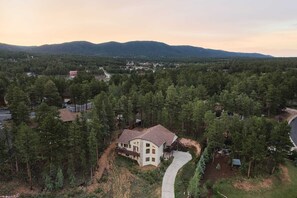 Une maison à deux étages, dotée d’une allée sinueuse, entourée d’une forêt dense et avec des montagnes en toile de fond.