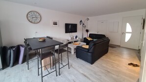 A modern living room with a dining table, black sofa, and a flat-screen TV. - House Bormes les Mimosas 100 m from shops and 200 m from the beach on foot (Bormes-les-Mimosas)