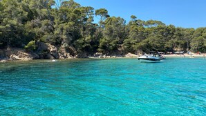A boat on a turquoise sea with a rocky coastline and dense trees in the background. - House Bormes les Mimosas 100 m from shops and 200 m from the beach on foot (Bormes-les-Mimosas)
