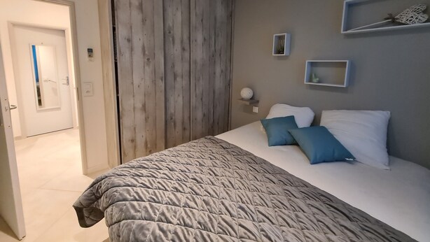 A bedroom with a bed, a wooden wardrobe, a door, and a shelf with decorative items. - House Bormes les Mimosas 100 m from shops and 200 m from the beach on foot (Bormes-les-Mimosas)