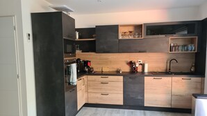 A modern kitchen with a black and wood finish, built-in appliances, and a small stool. - House Bormes les Mimosas 100 m from shops and 200 m from the beach on foot (Bormes-les-Mimosas)