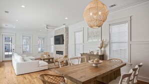 A spacious living room with a large wooden dining table, white sofas, and wicker chairs.