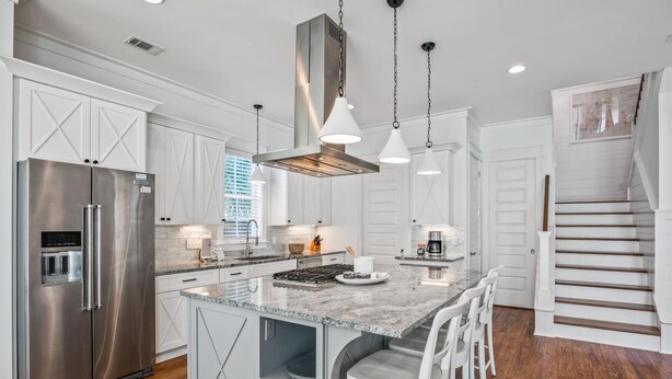A modern kitchen with a stainless steel refrigerator, granite countertops, and a central island with bar stools.