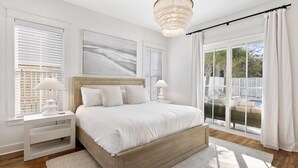 A bedroom with a large bed, a nightstand, a chandelier, and a view of a pool through large windows.