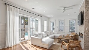 A spacious living room with a white sectional sofa, wicker chairs, and a fireplace.