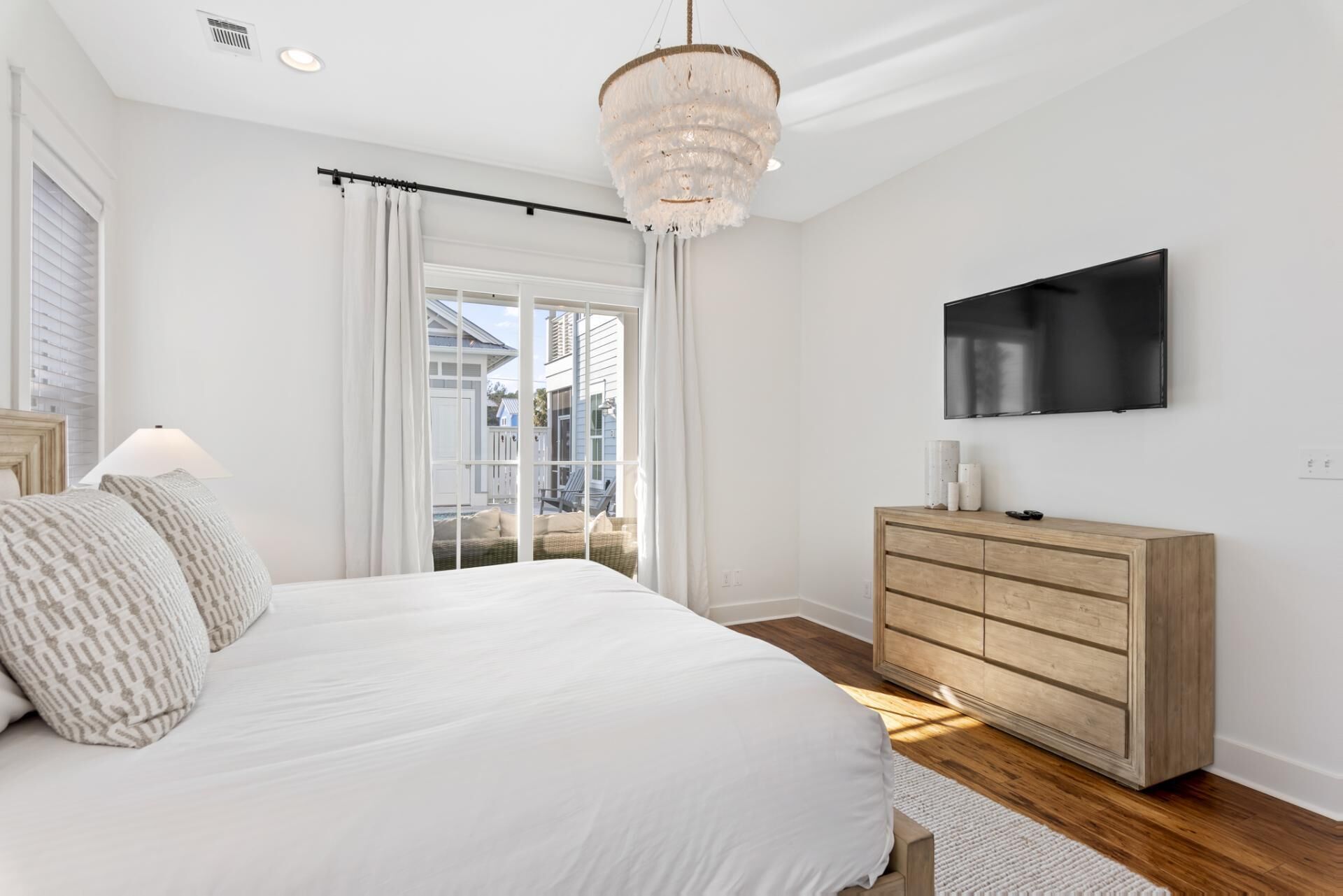 Un dormitorio con una cama grande, un aparador de madera, un televisor montado en la pared y una ventana con cortinas.