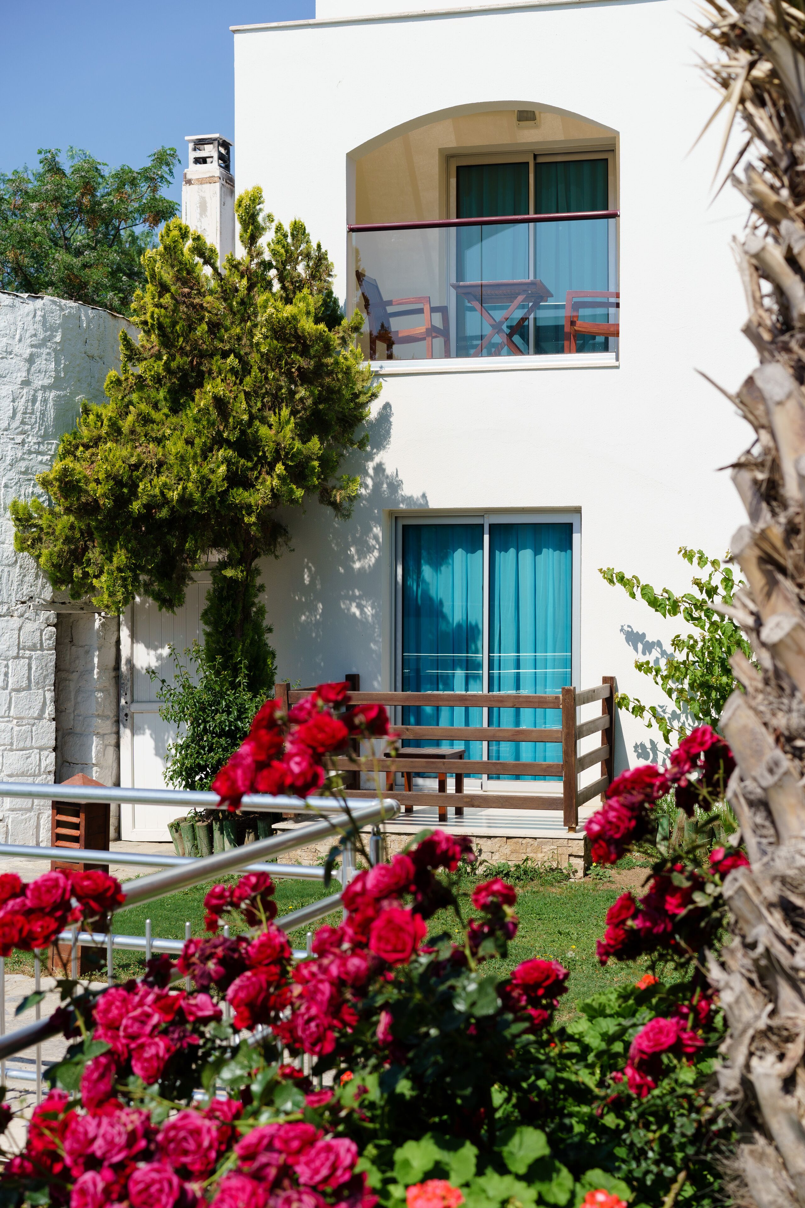 A two-story building with a balcony, a stone wall, and a tree.