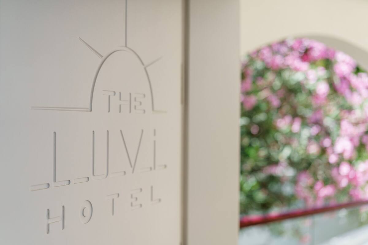 Señal de hotel con el nombre "THE LUV HOTEL" y una vista parcial de un arco floral rosa.