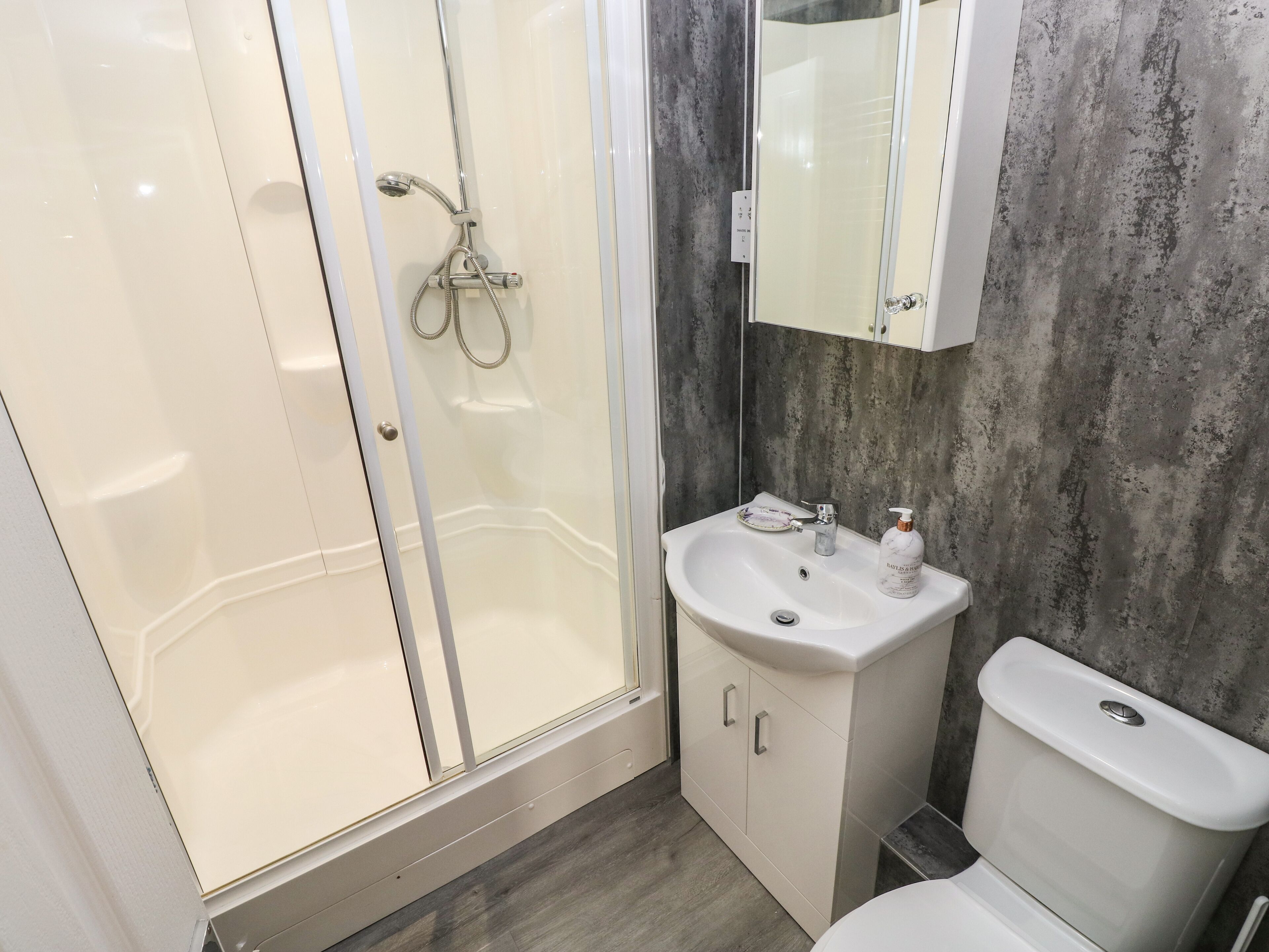 A bathroom with a glass-enclosed shower, a white sink with a mirror above it, and a toilet.