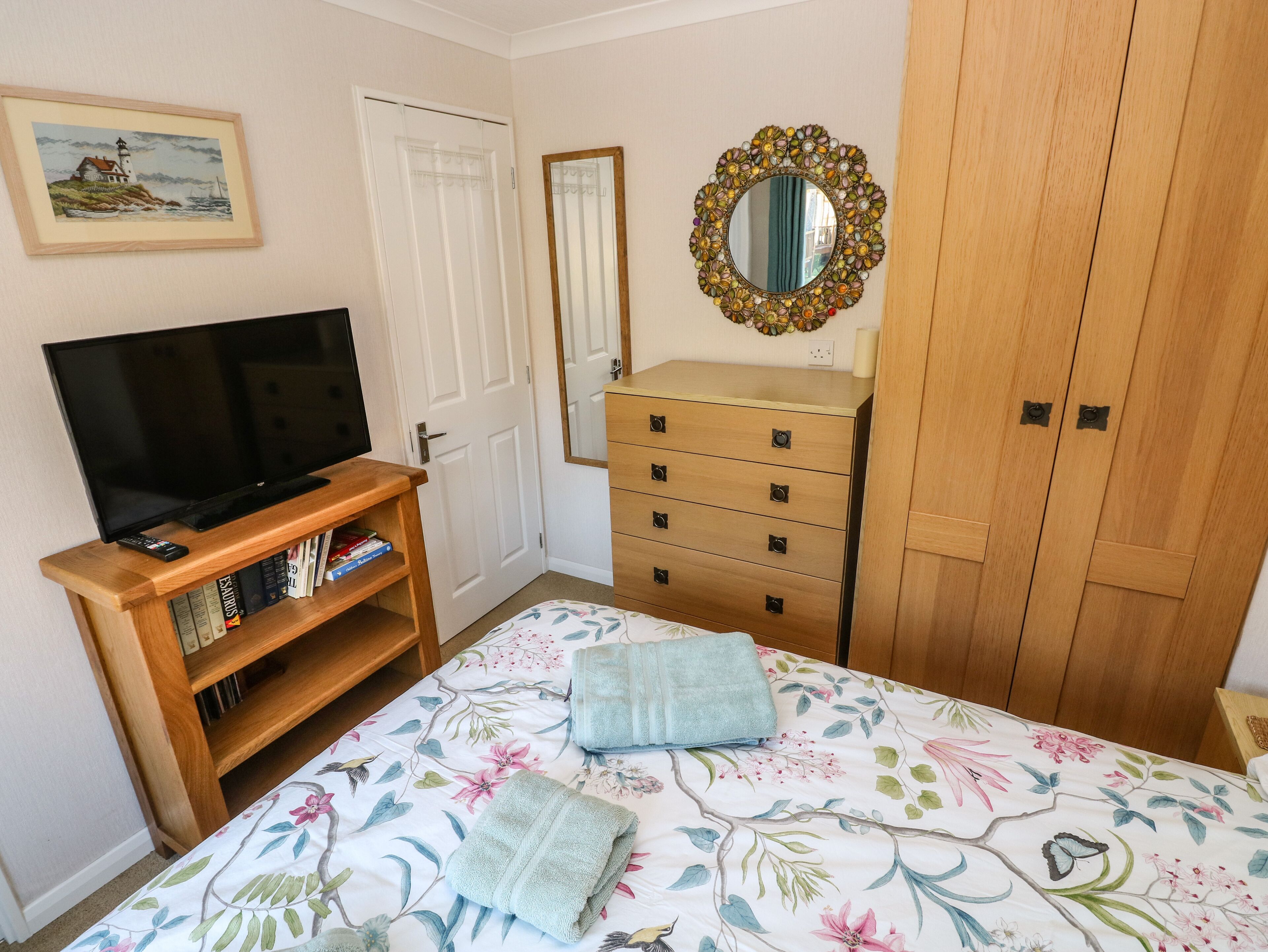 A bedroom with a bed, a dresser, a television on a stand, a mirror with a decorative frame, and a door.