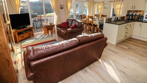 Een ruime woonkamer met een leren bank, een televisie en een eettafel met stoelen.