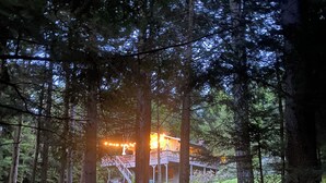 A forested area with a dirt path leading to a building with a deck. - Bayou Chalet – Your Perfect Getaway Near Sugarbush Resort (Warren)