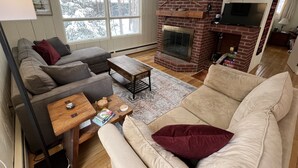 A cozy living room with a fireplace, two sofas, a coffee table, and a TV. - Bayou Chalet – Your Perfect Getaway Near Sugarbush Resort (Warren)