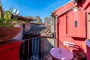 Ein rotes Gebäude mit einem Ziegeldach, einem kleinen Balkon mit Tisch und Stühlen sowie einem Blumentopf.