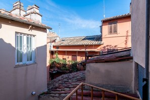 Ein schmaler Gang mit terrakottafarbenen Dächern, einer Holztreppe und einem Gebäude mit vergittertem Fenster.