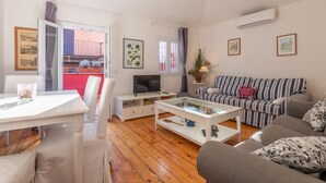 Ein Wohnzimmer mit Sofa, Fernseher, Couchtisch und einem Essbereich mit Stühlen und Tisch.