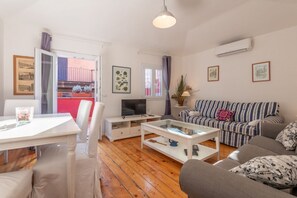 Ein Wohnzimmer mit Sofa, Fernseher, Couchtisch und einem Essbereich mit Stühlen und Tisch.