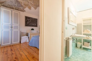 Une chambre comprenant un lit, une commode, un panneau fixé au mur, et une salle de bain avec un lavabo et un porte-serviettes.