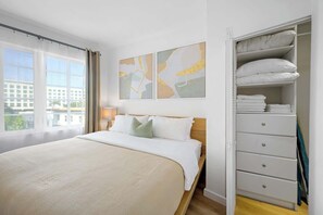 A hotel room with a large bed, a wardrobe with multiple drawers, and a window with a view of buildings. - Oceanfront Junior 2BR APT on Ocean Drive (Miami Beach)