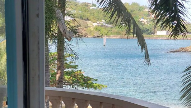 Vista de un cuerpo de agua tranquilo con una boya distante, rodeado de vegetación y edificios.