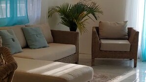 Una sala de estar con un sofá color beige, un sillón de mimbre y una planta en maceta.