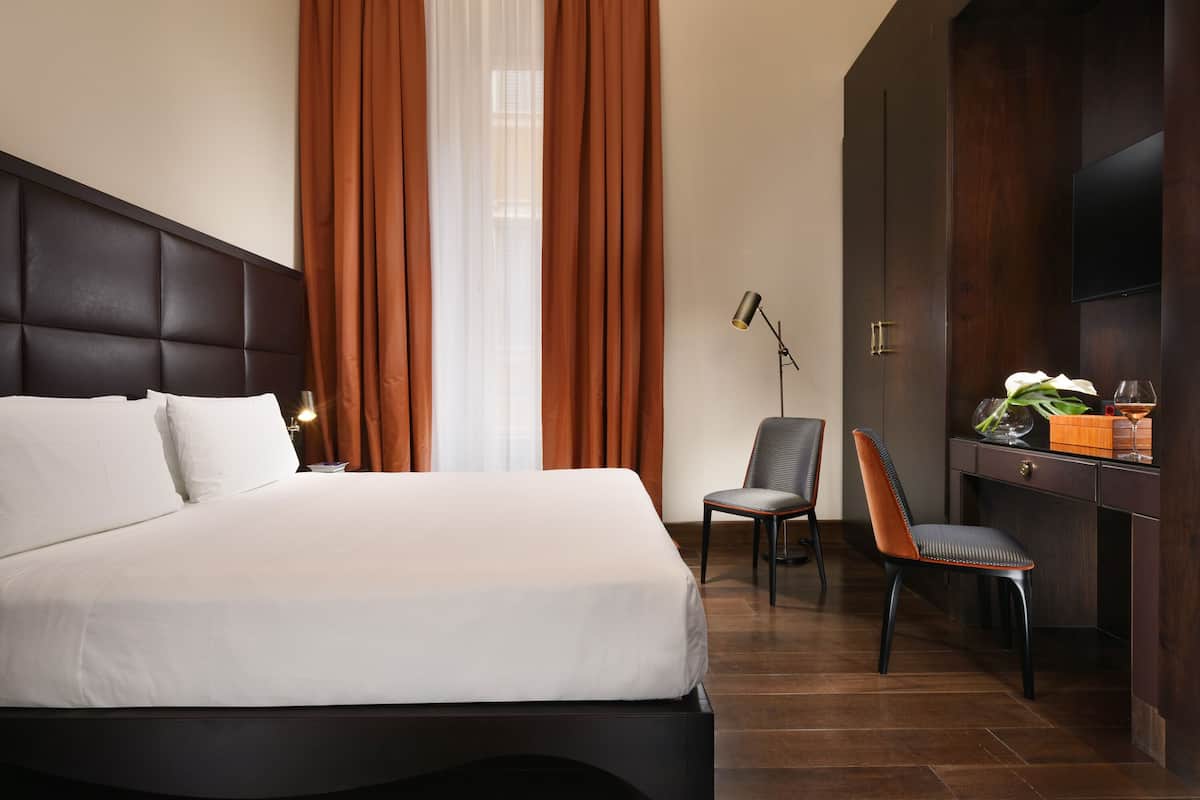 A hotel room with a large bed, a desk with a chair, a TV, and a window with curtains.