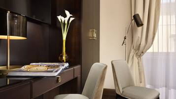 Une chambre d’hôtel avec un bureau en bois foncé, une lampe, un vase avec des fleurs blanches et deux fauteuils rembourrés.