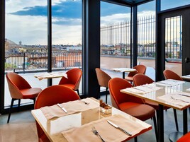 Un restaurant avec des chaises et des tables rouges, et de grandes fenêtres donnant sur la ville.