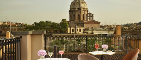 A terrace with round tables and wicker chairs, overlooking a historic building with a dome.