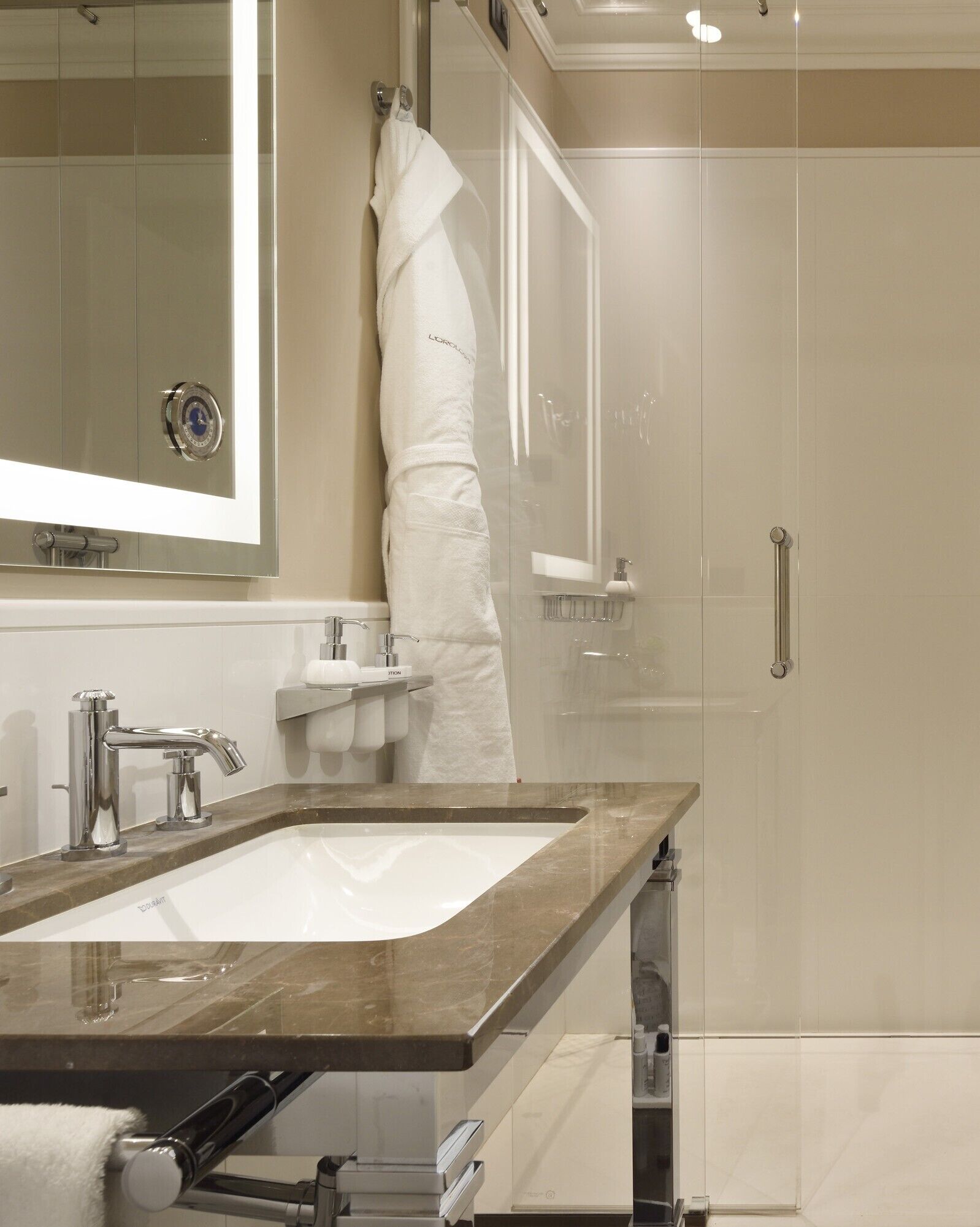 Un baño moderno con un espejo grande, un lavamanos con encimera de mármol, una cabina de ducha de vidrio y un perchero para toallas.
