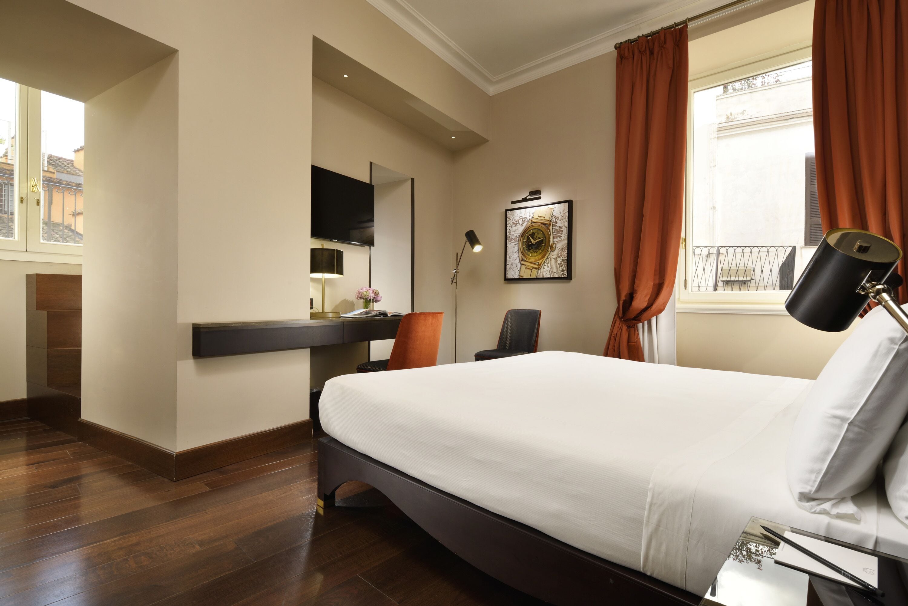 Una habitación de hotel con una cama grande, un escritorio con ordenador, una silla, un televisor montado en la pared y una ventana con cortinas.