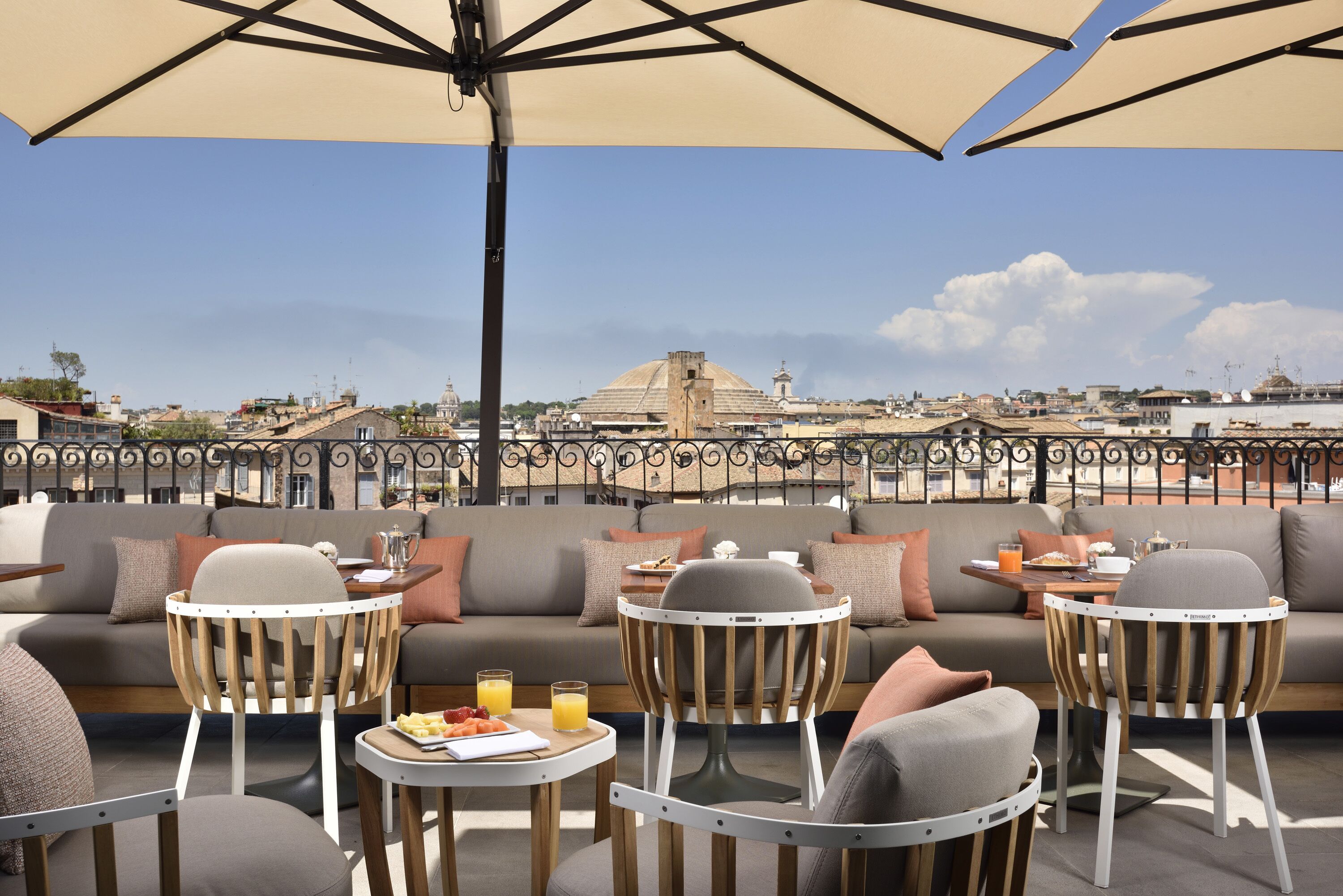A rooftop terrace with a sofa set, chairs, and tables, overlooking a cityscape with a prominent dome structure.