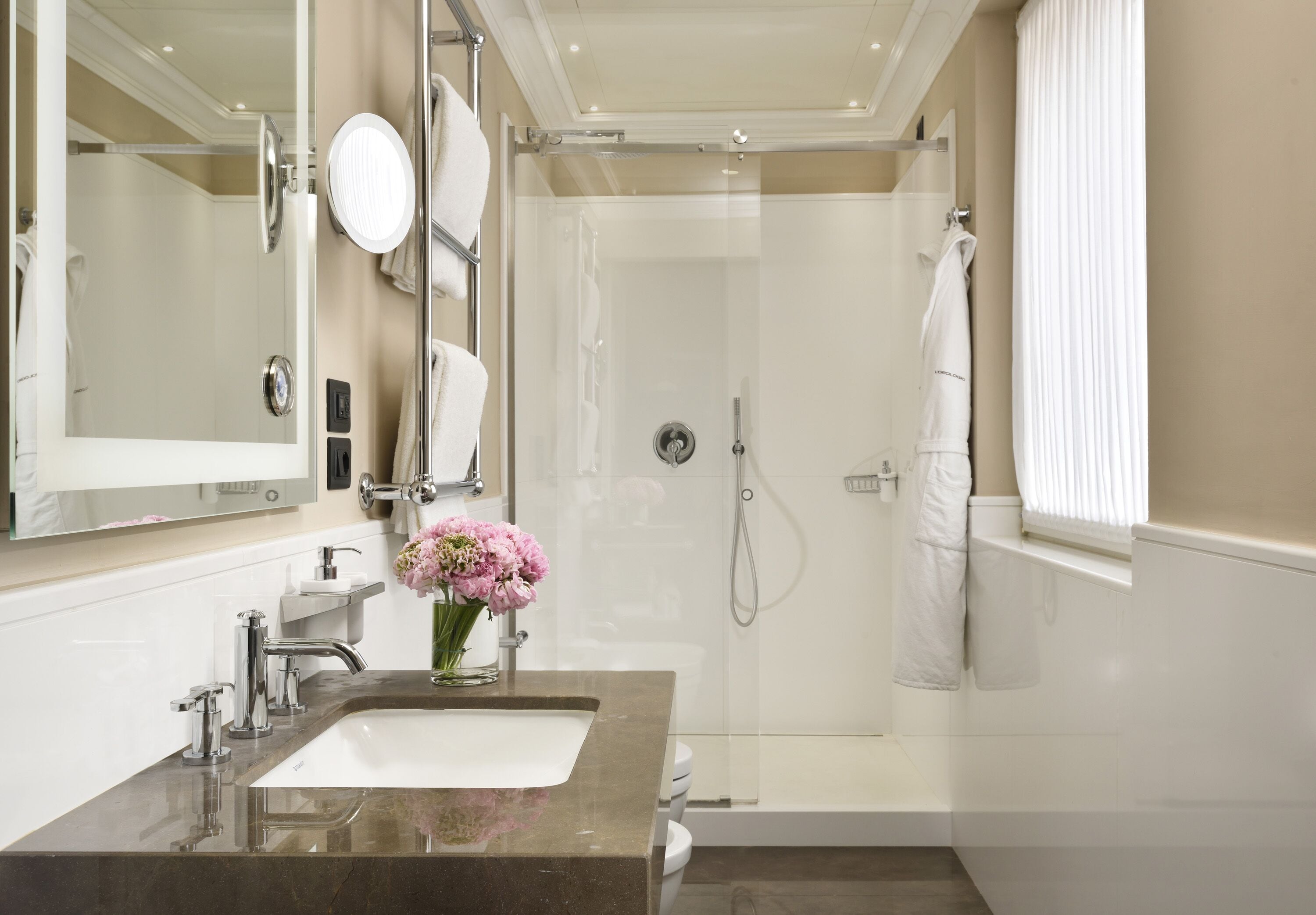 Un baño moderno con un espejo grande, un lavamanos, una ducha y una ventana con persianas.