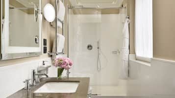 Un baño moderno con un espejo grande, un lavamanos, una ducha y una ventana con persianas.