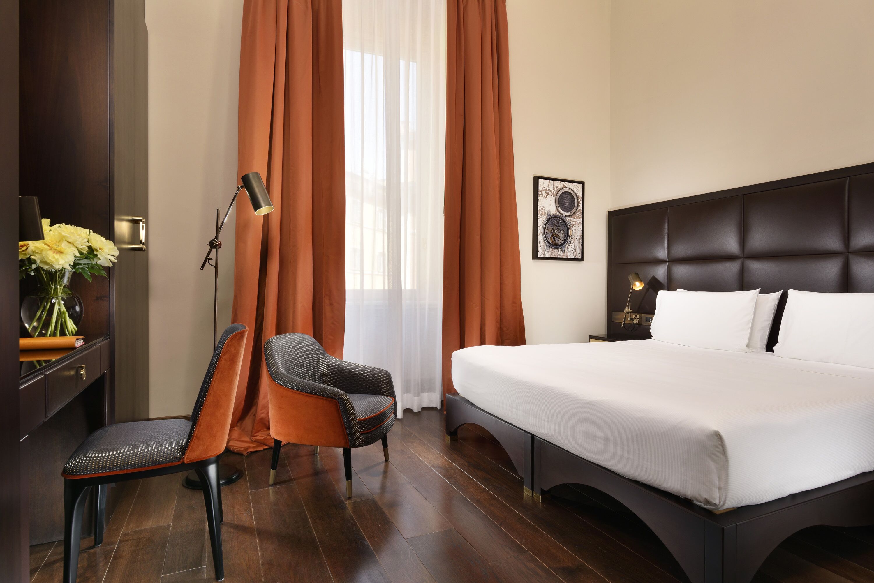A hotel room with a bed, a chair, a desk, a lamp, and a window with curtains.