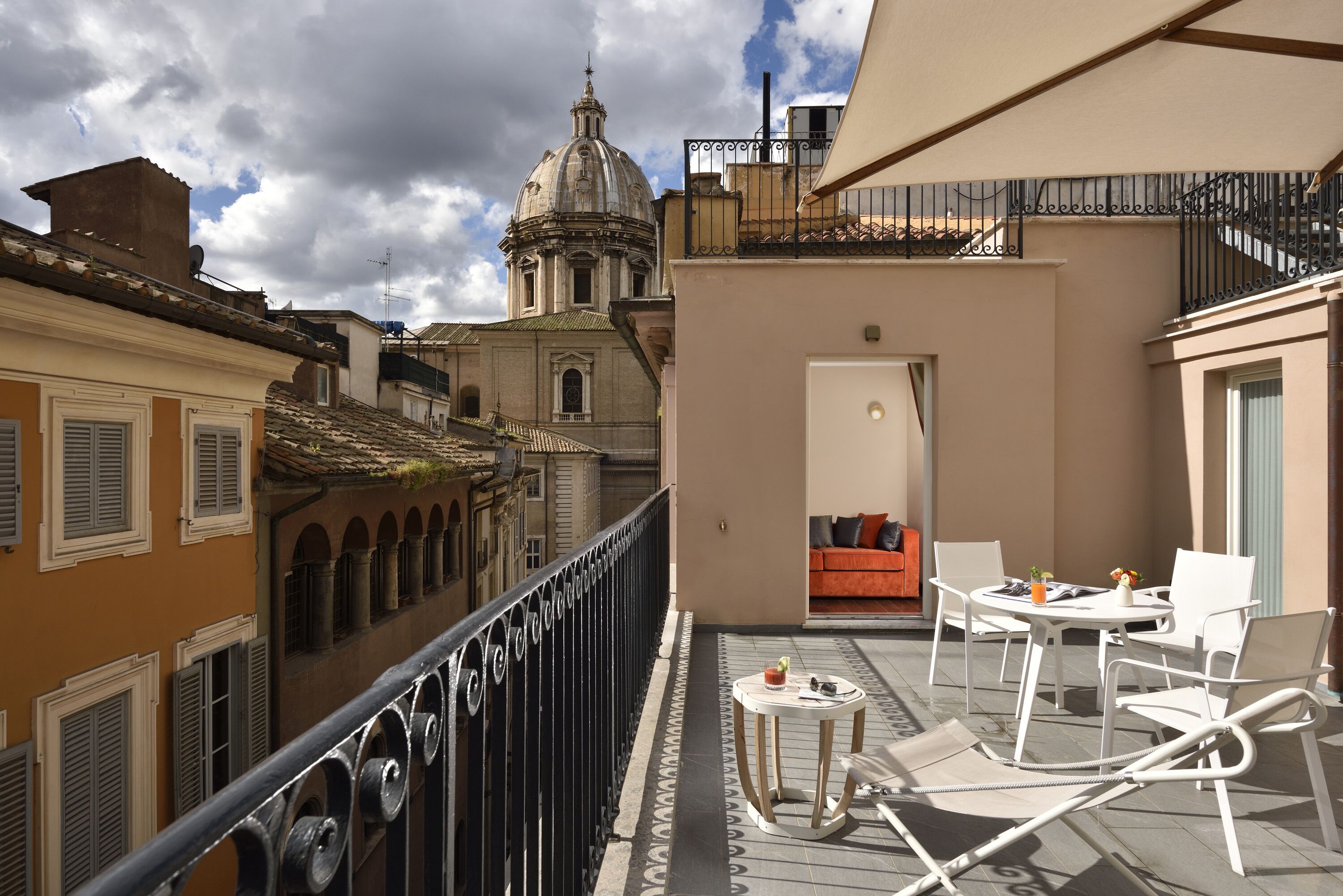 A balcony with a white table and chairs, a small round table with a bottle and glasses, and a view of a historic building with a dome.