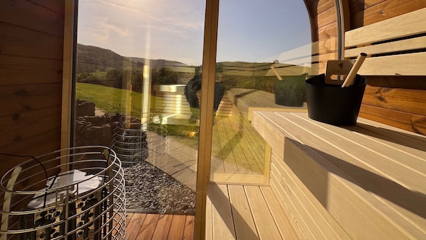 A wooden cabin with a glass door leading to a deck with a view of a green landscape. - Bretherdale Barn (Bretherdale)
