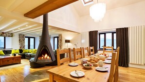 A spacious living room with a large wooden dining table, a fireplace, and a cozy seating area with a sofa and chairs. - Bretherdale Barn (Bretherdale)
