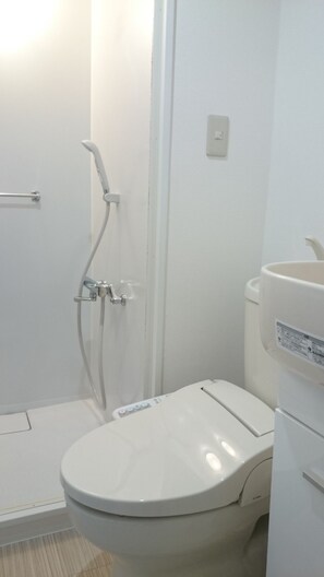 Un baño pequeño y blanco con inodoro, ducha y lavabo.